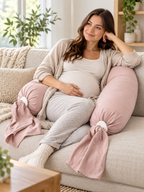 Blush pink adjustable pregnancy pillow supporting a seated adult on a modern sofa