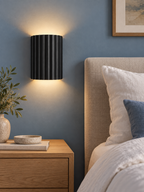 Black resin up and down wall light beside a modern bed
