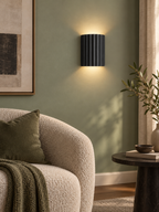Black fluted wall sconce in a sage green reading corner