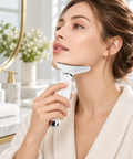 Woman using a white face and neck massager beneath her jaw in a bright bathroom