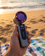 Handheld personal fan in use on a beach, golden hour