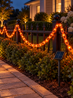 Orange solar chain string lights installed along a garden fence